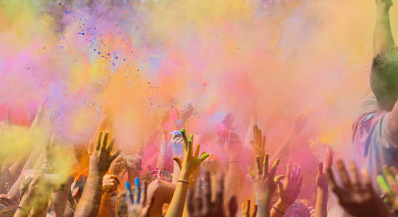 People enjoying the colorful Holi festival in Barcelona a indian tradition to welcome the spring covering himself of gulal powder, moment when all the crowd throwing the colorful powder to the air with arms raised. Catalonia, Europe.