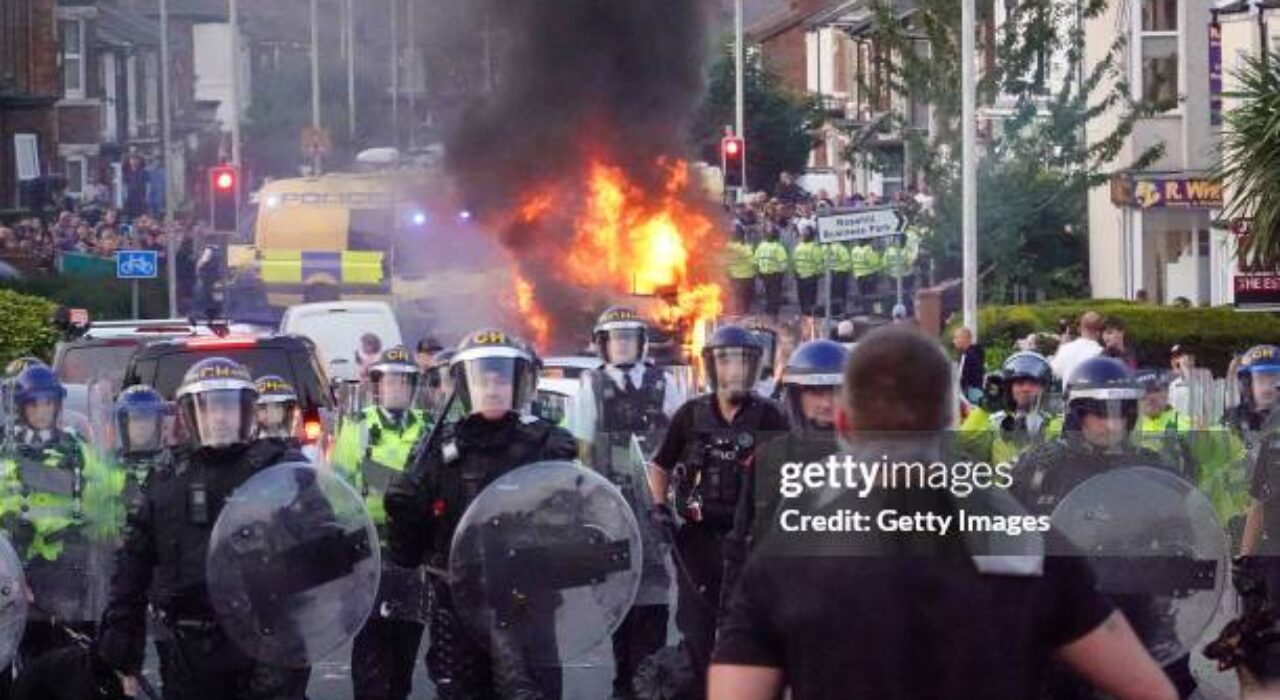 SOUTHPORT, ENGLAND - JULY 30: Riot police hold back protesters near a burning police vehicle after disorder broke out on July 30, 2024 in Southport, England. Rumours about the identity of the 17-year-old suspect in yesterday's deadly stabbing attack here have sparked a violent protest. According to authorities and media reports, the suspect was born in Cardiff to Rwandan parents, but the person cannot be named due to his age. A false report had circulated online that the suspect was a recent immigrant who crossed the English Channel last week and was "on an MI6 watchlist." (Photo by Getty Images/Getty Images)